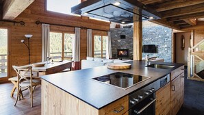 A modern kitchen with a central island, built-in stove, and stone accents. - Authentic Swiss Spa Chalet Hot Tub & Sauna (Riddes)