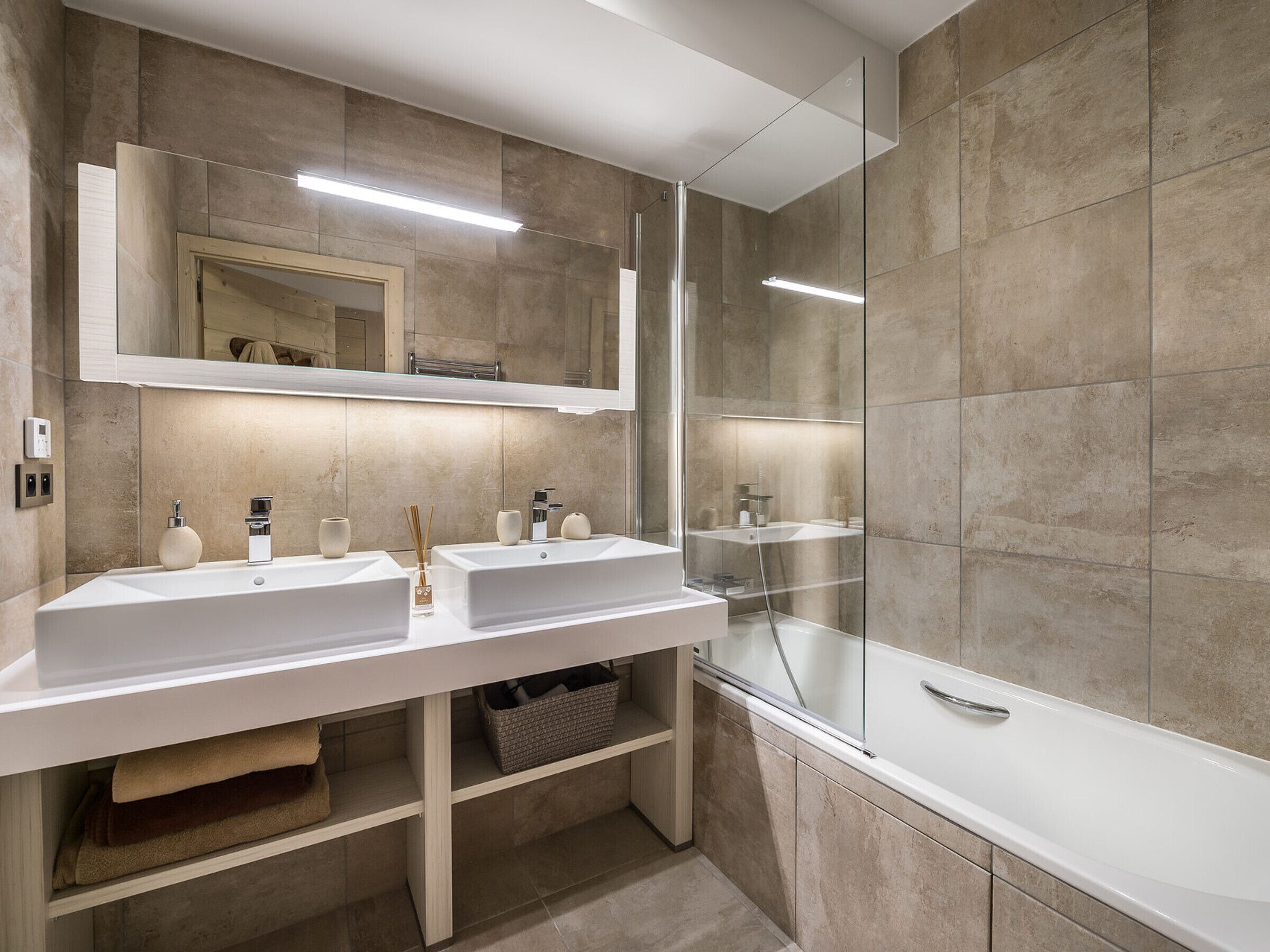 Een moderne badkamer met twee wasbakken, een grote spiegel en een douche met glazen wanden.
