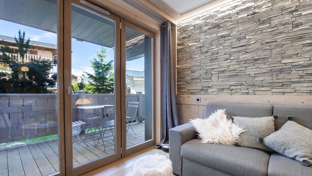 A modern living room with a stone wall, a grey sofa, and a fluffy white stool. - Family apartment in central Courchevel with parking and wifi (Courchevel 1550)
