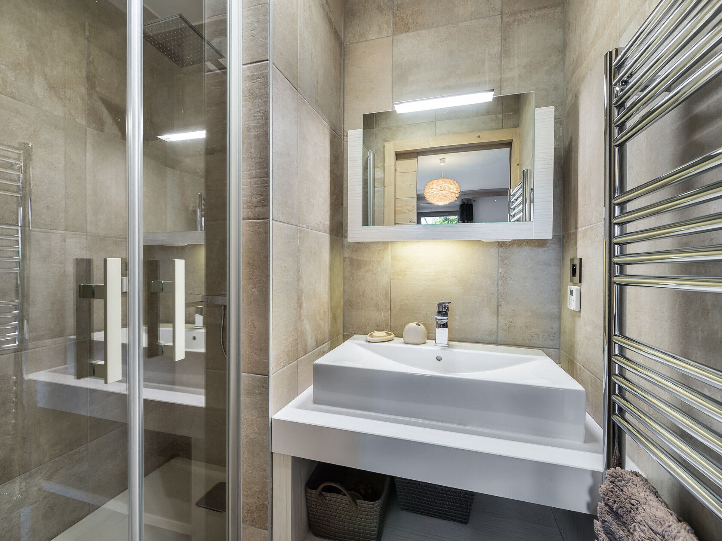 A modern bathroom with a glass shower enclosure, a white sink with a mirror above, and a towel rack on the right.