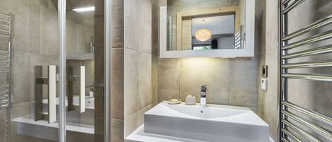 A modern bathroom with a glass shower enclosure, a white sink with a mirror above, and a towel rack on the right.