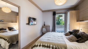 A bedroom with two beds, a large mirror, a television, and a window with a view of greenery. - Family apartment in central Courchevel with parking and wifi (Courchevel 1550)