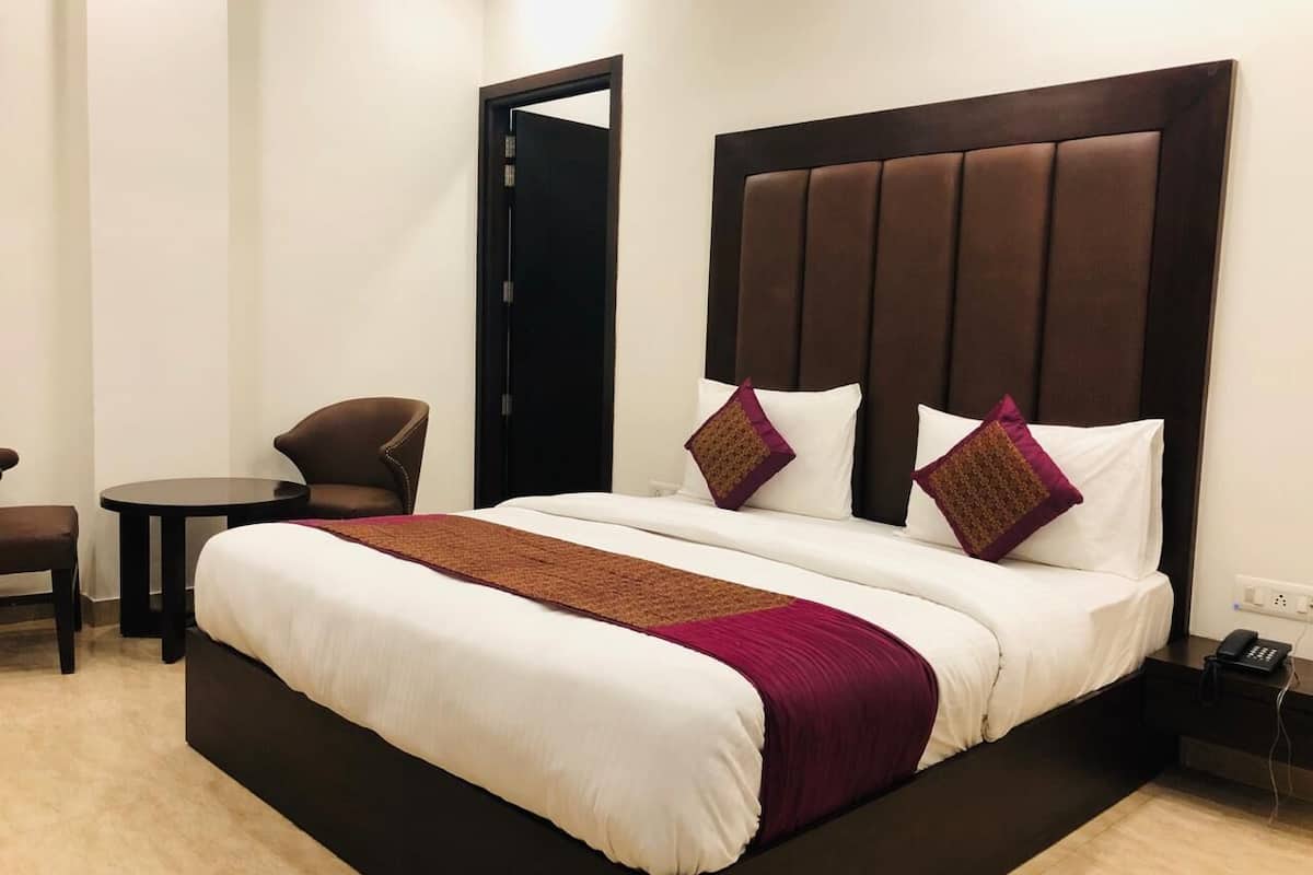 Uma cama grande com cabeceira escura, dois travesseiros, um cobertor marrom e uma mesinha de cabeceira com um telefone.