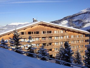 A multi-story wooden building with balconies, surrounded by snow-covered trees and mountains.