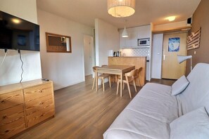 A modern living room with a sofa, wooden dining table, and a TV mounted on the wall.
