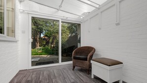 Ein Zimmer mit einer Schiebetür zum Garten, ein Korbsessel mit brauner Sitzauflage und eine weiße Bank.