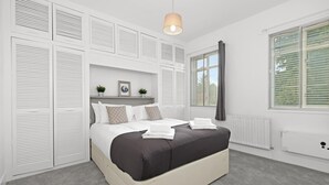Ein Schlafzimmer mit einem Bett, weißen Fensterläden, einem Heizkörper und einem fensterbepflegten Fenster.