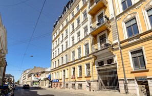 A multi-story building with a yellow facade, multiple balconies, and a cobblestone street.
