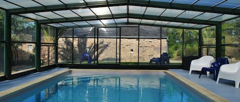 Una piscina interior amb parets de vidre transparent, parets de pedra i zones de seients.