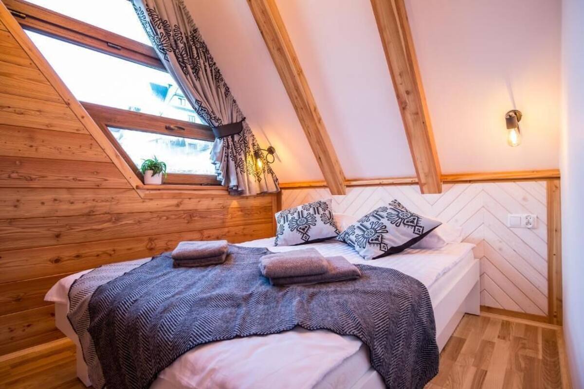 Een gezellige slaapkamer met een schuine kap, houten wanden, een bed met opvallende kussens en een raam met gordijnen.