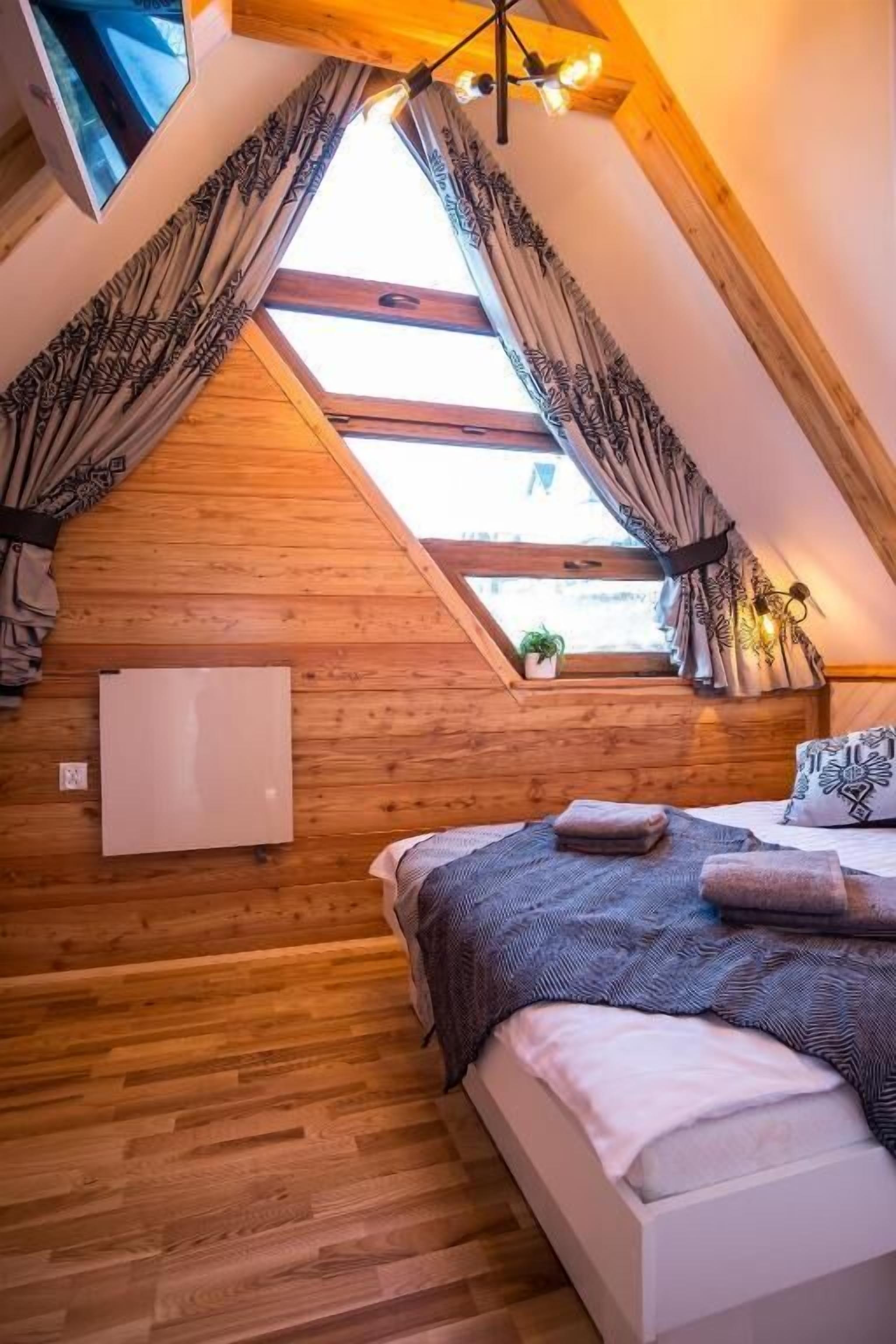 Une chambre mansardée chaleureuse avec des murs en bois, une lucarne, un lit avec une literie à motifs et une petite plante en pot.
