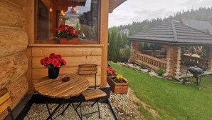 Una cabaña de madera con un patio amueblado, una ventana adornada con flores y vista a un área boscosa.