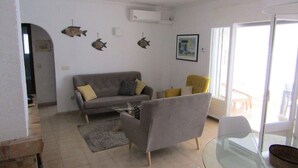 En stue med sofa, lænestol, glasbord og et spiseområde med stol og bord.