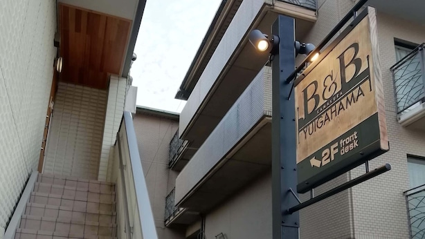 A building with a sign for B&B YUIGAHAMA, a 2F front desk, and a gated entrance. - B&B Yuigahama (Kamakura)