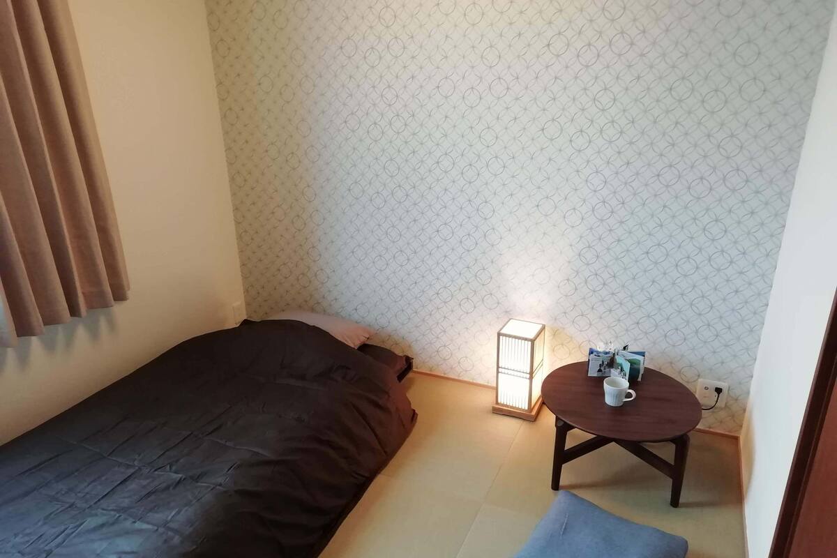 Ein kleines Zimmer mit einem Bett, einem Nachttisch mit einer Lampe und einem blauen Kissen.