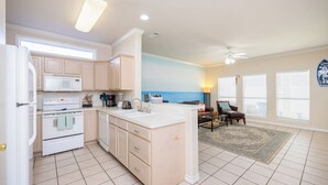 A kitchen with a central island, white appliances, and a dining area with a view of the ocean. - Spacious family home with patio, steps away from the beach with a pool onsight! (Corpus Christi)