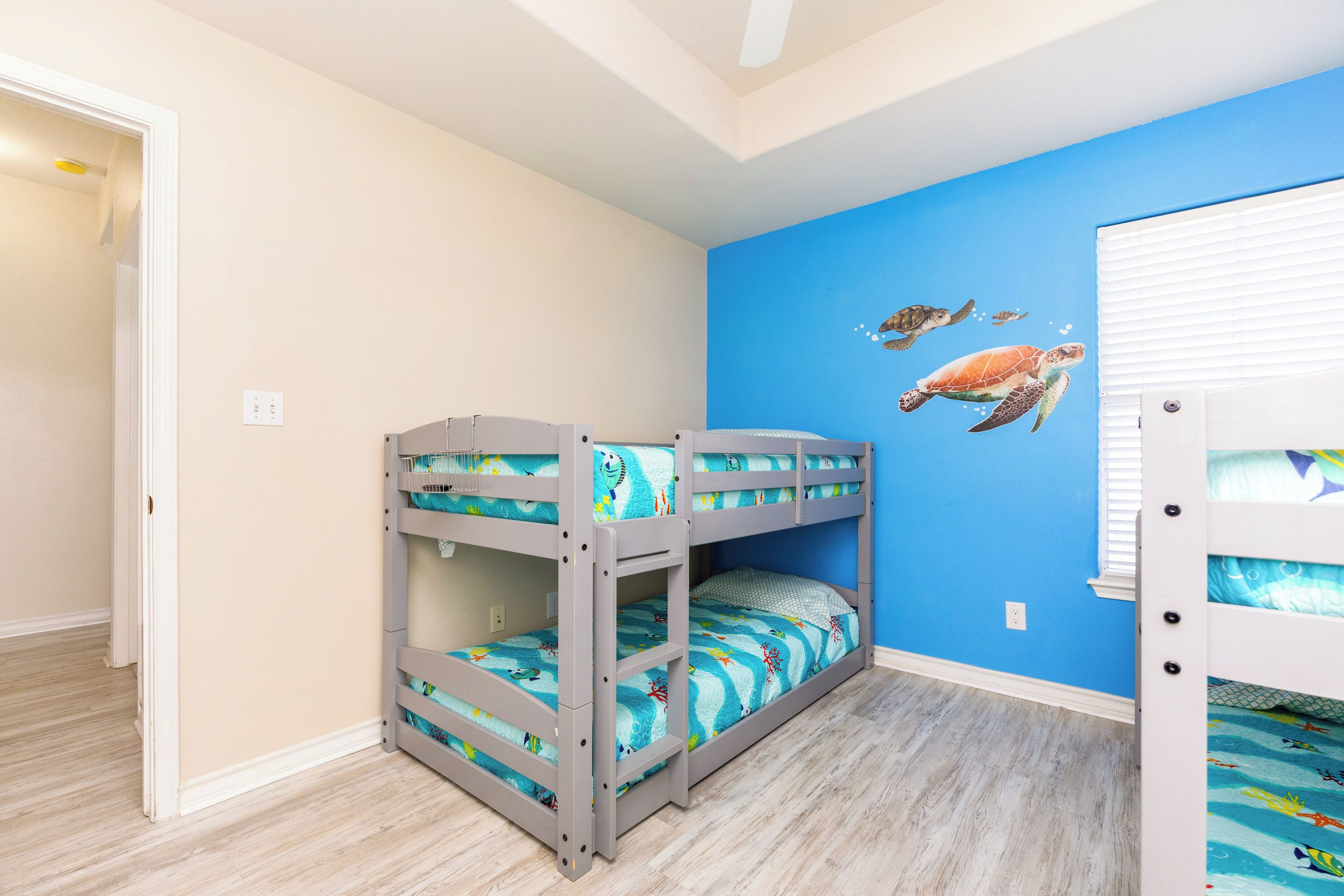 A room with bunk beds, a blue wall with sea turtle decals, and wooden flooring.