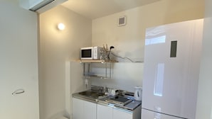 A compact kitchen with white cabinets, a microwave, a refrigerator, and a sink. - B&B Kamakura (Kamakura)