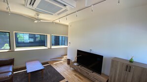 A modern living room with a flat-screen TV, wooden flooring, and large windows. - B&B Kamakura (Kamakura)