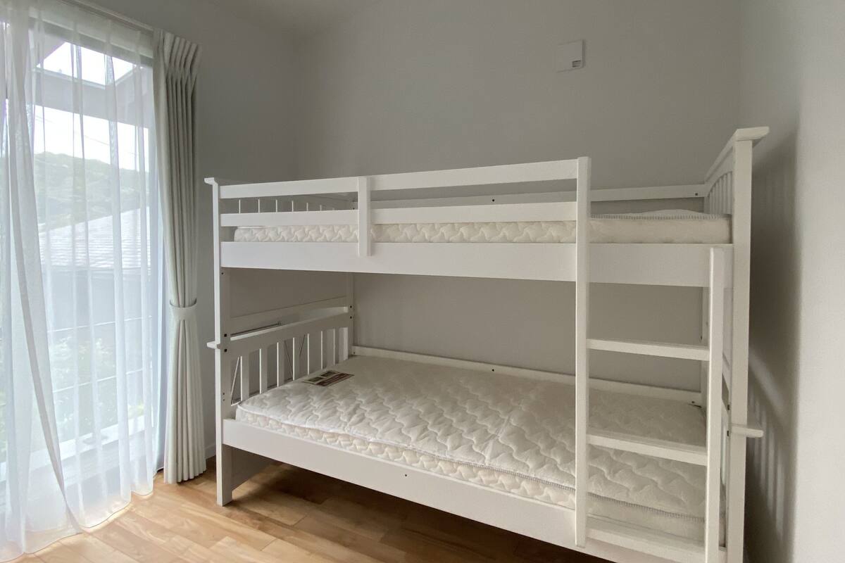 A bunk bed room with a wooden floor, white walls, and a window with curtains.