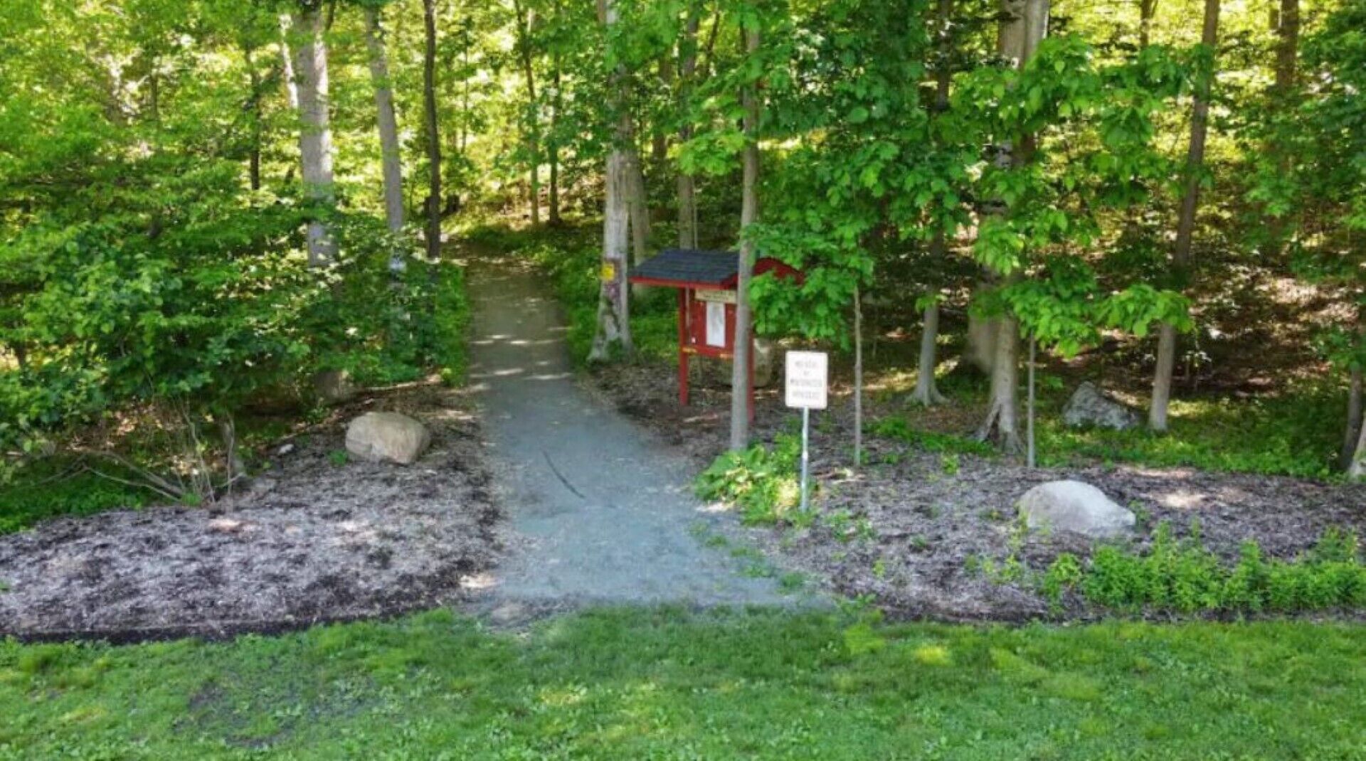A forested area with a small red structure, possibly a shelter or information point, near a dirt path.