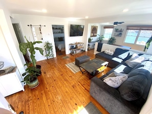 Un salon spacieux avec un canapé gris, un plancher en bois et un téléviseur fixé au mur.