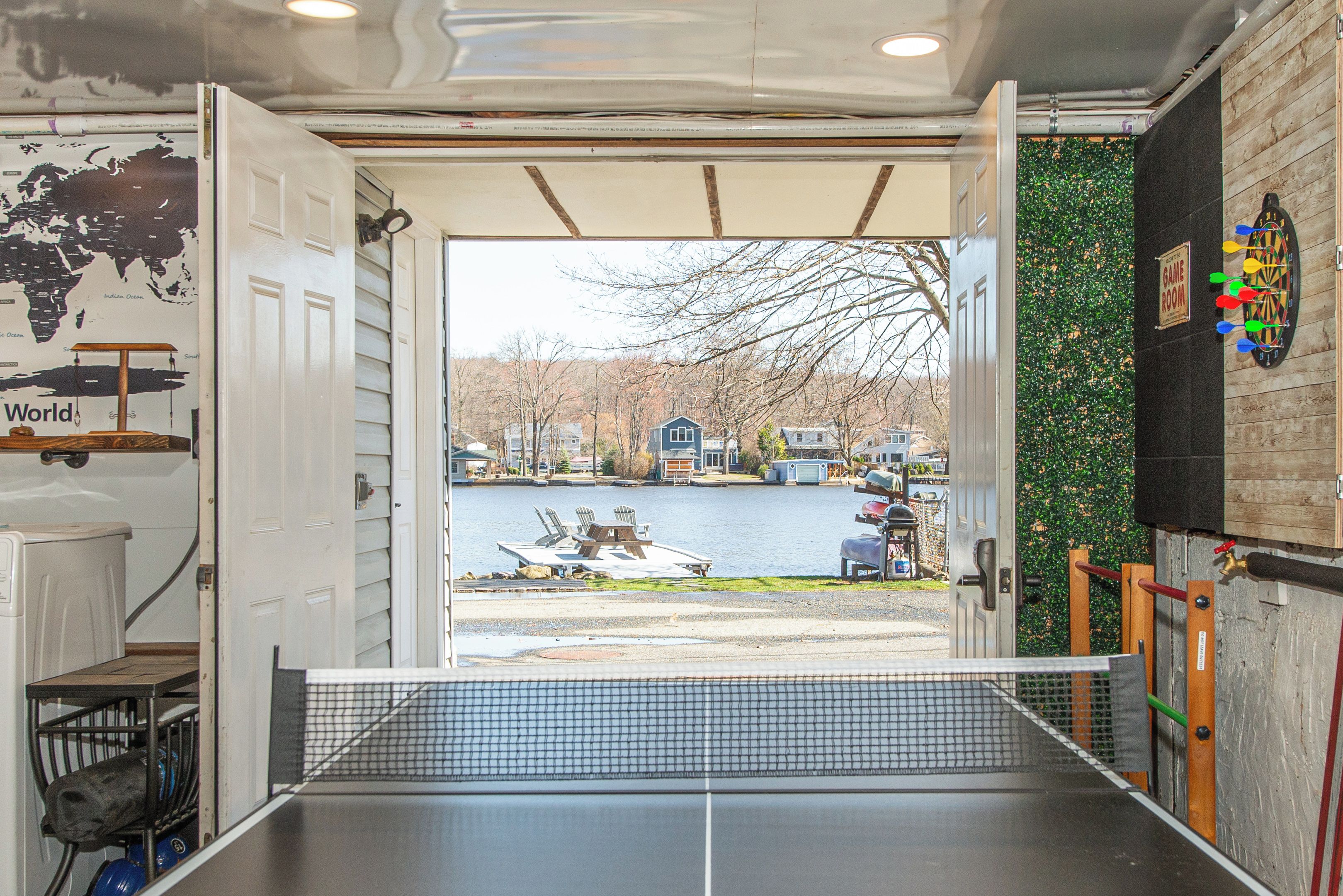 Une table de ping-pong installée à l’intérieur, avec vue sur un lac et des maisons en arrière-plan.