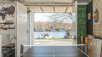Une table de ping-pong installée à l’intérieur, avec vue sur un lac et des maisons en arrière-plan.