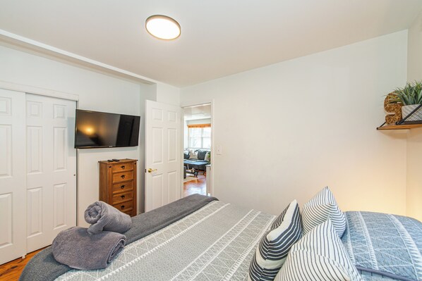 A bedroom with a bed, a television, a dresser, and a hallway leading to another room. - Lake Hopatcong Lake House - Private Dock, Game Room, kayaks, canoe and Grill (Lake Hopatcong)