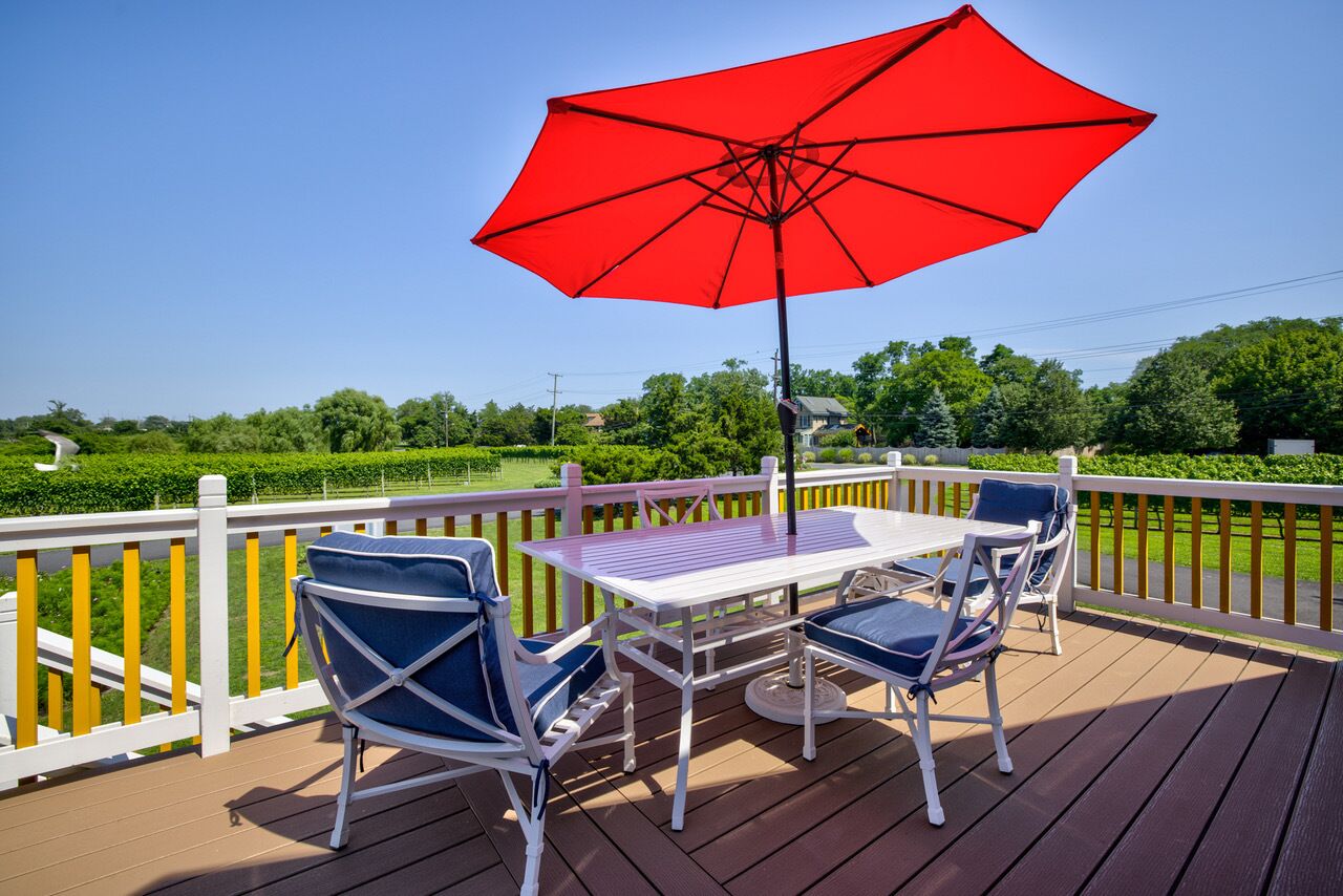 Une terrasse avec une table et des chaises, un parasol rouge et une rambarde blanche.