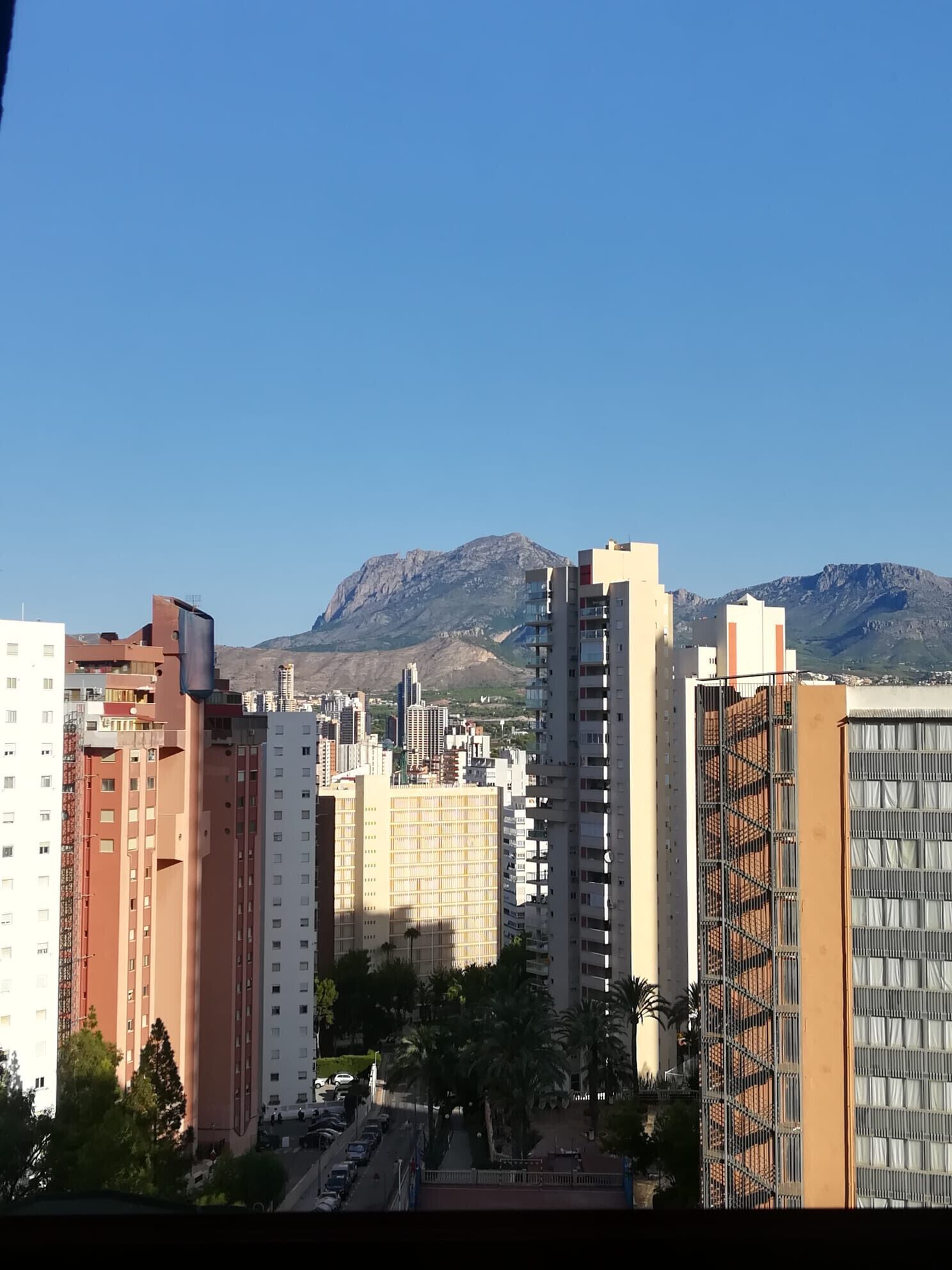A cityscape with modern high-rise buildings, a clear sky, and mountains in the background.