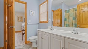 Une salle de bain avec un lavabo blanc, des meubles en bois, des toilettes et un rideau de douche.