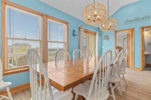 A dining area with a wooden table and white chairs, large windows with blinds, and a decorative hanging light fixture.