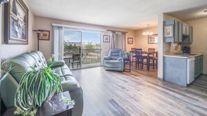 Een woonkamer met een bank, een eettafel met stoelen, een keuken met kastjes, en een balkon met uitzicht.