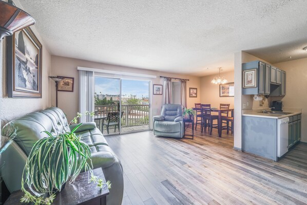 A living room with a sofa, a dining table with chairs, a kitchen area with cabinets, and a balcony with a view.