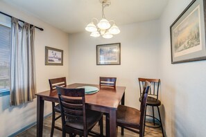 A dining area with a wooden table, four chairs, a chandelier, and framed pictures on the walls.
