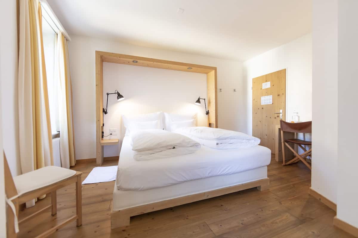 A neatly made bed with white linens, a wooden headboard, and two bedside lamps.