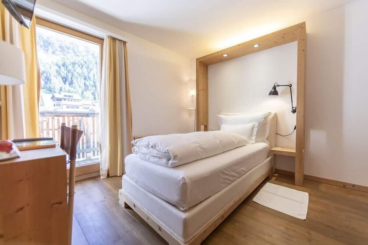 A bedroom with a bed, bedside lamp, wooden headboard, and a view of a balcony.