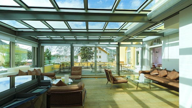 A sunlit room with a glass ceiling, a sofa, chairs, and a glass table. - Hotel Müller Mountain Lodge (Pontresina)