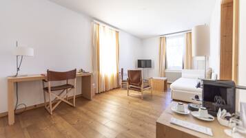 A modern hotel room with a wooden desk, a comfortable chair, a bed, and a television.