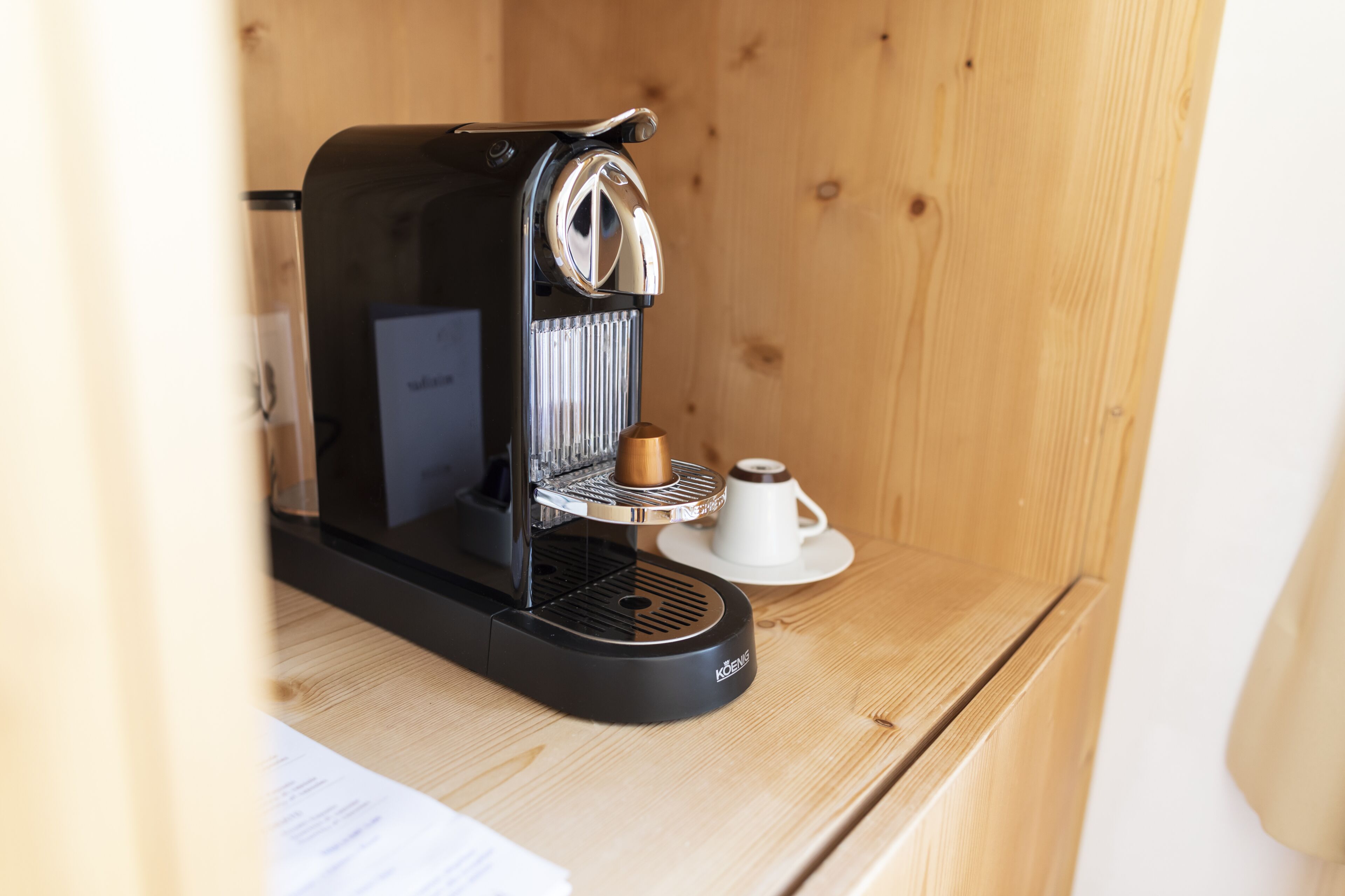 A compact coffee machine on a wooden surface with a cup and saucer nearby.