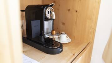 A compact coffee machine on a wooden surface with a cup and saucer nearby.