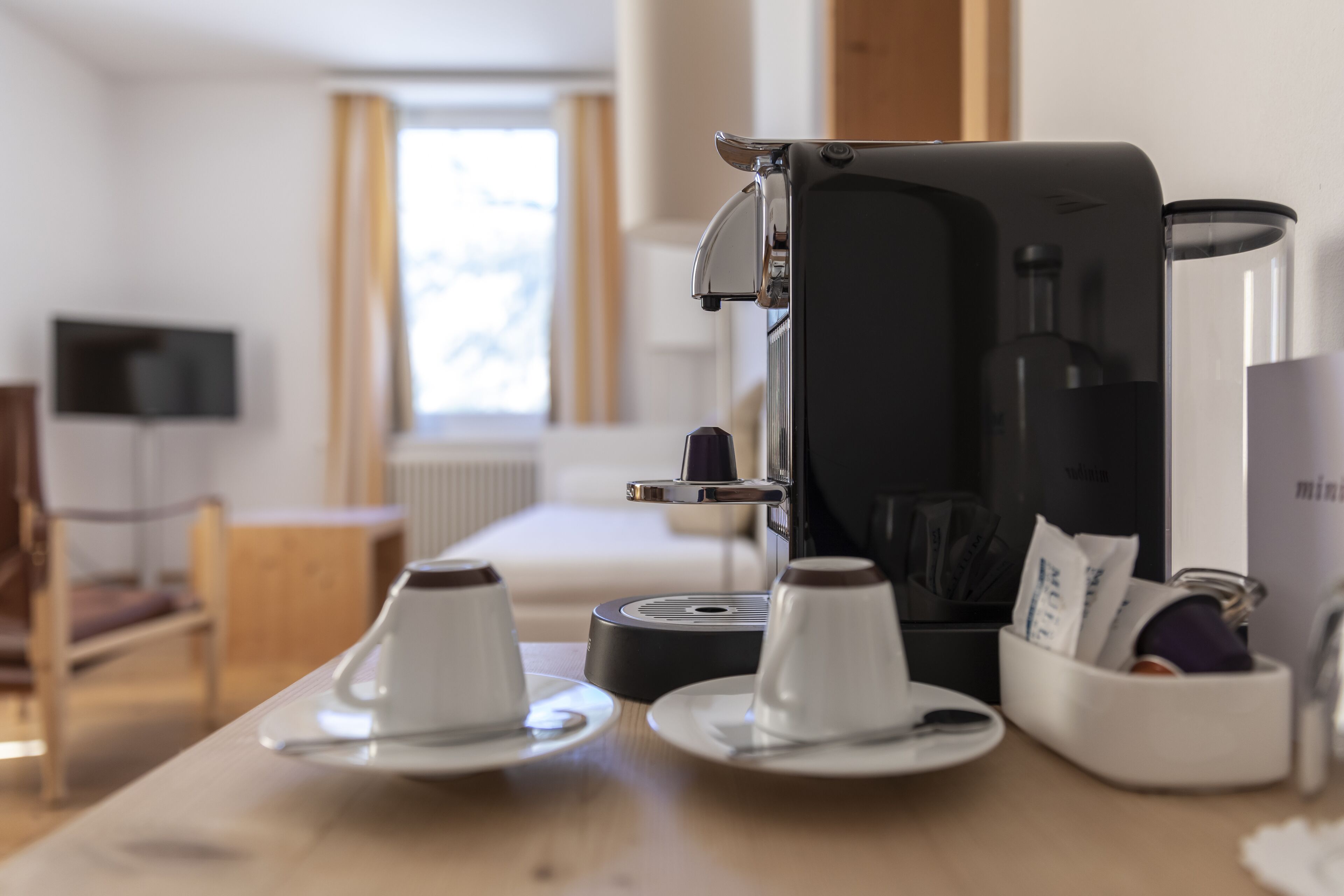 Una cafetera sobre una mesa con dos tazas y un recipiente pequeño.