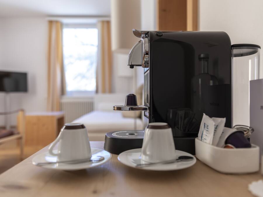 Una cafetera sobre una mesa con dos tazas y un recipiente pequeño.