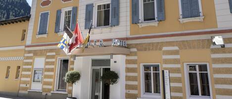 Ein Hotel mit gelber Fassade, zahlreichen Fenstern mit Fensterläden und einem Schild mit der Aufschrift "MÜLLER".