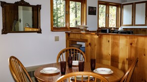 Una mesa de madera para comer con cuatro sillas, un armario de madera y una ventana con vistas a árboles.