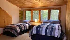 Un dormitorio con dos camas, techo de madera y vista a árboles a través de amplios ventanales.