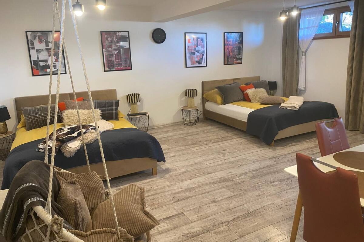 Habitación de hotel con dos camas, una silla colgante, zona de comedor y obras de arte en las paredes.