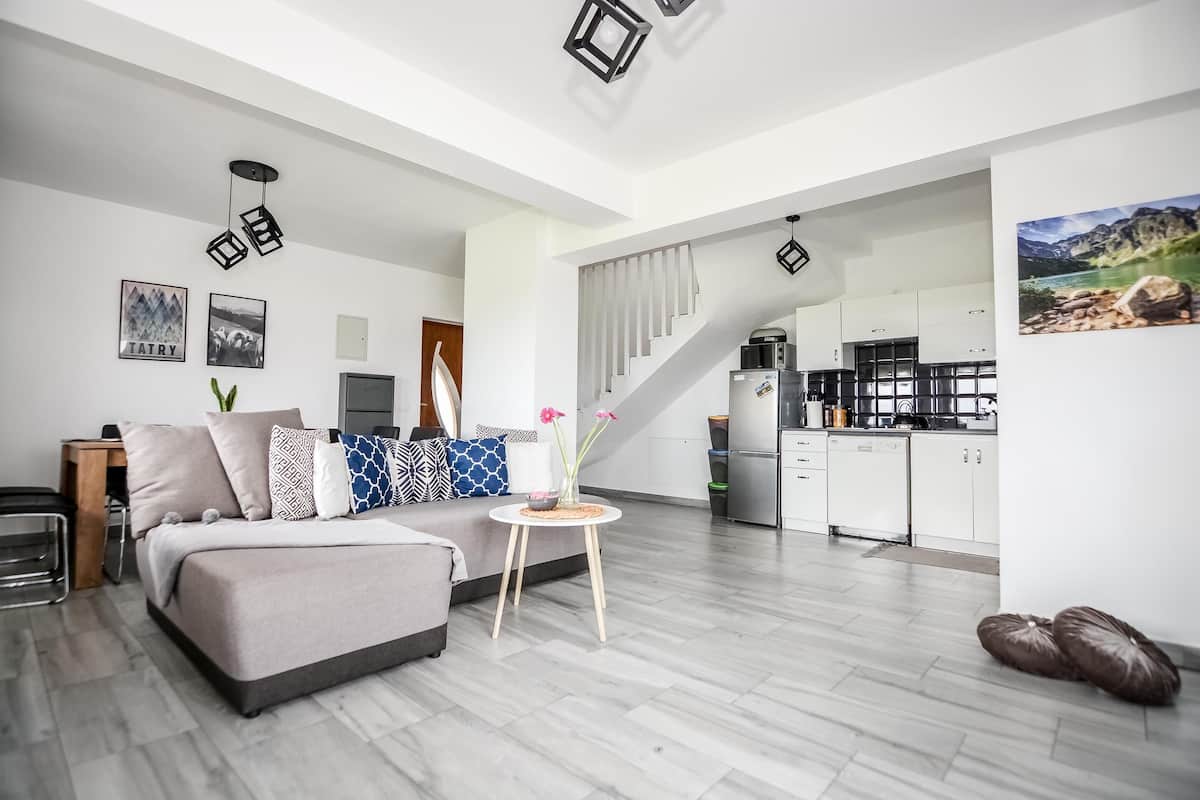 Una sala moderna con un sofá, una mesita redonda con un florero, y una escalera que sube a una cocina.