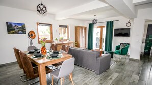 Een moderne woonkamer met een eethoek, een grijze bank, een houten eettafel en een aan de muur bevestigde televisie.